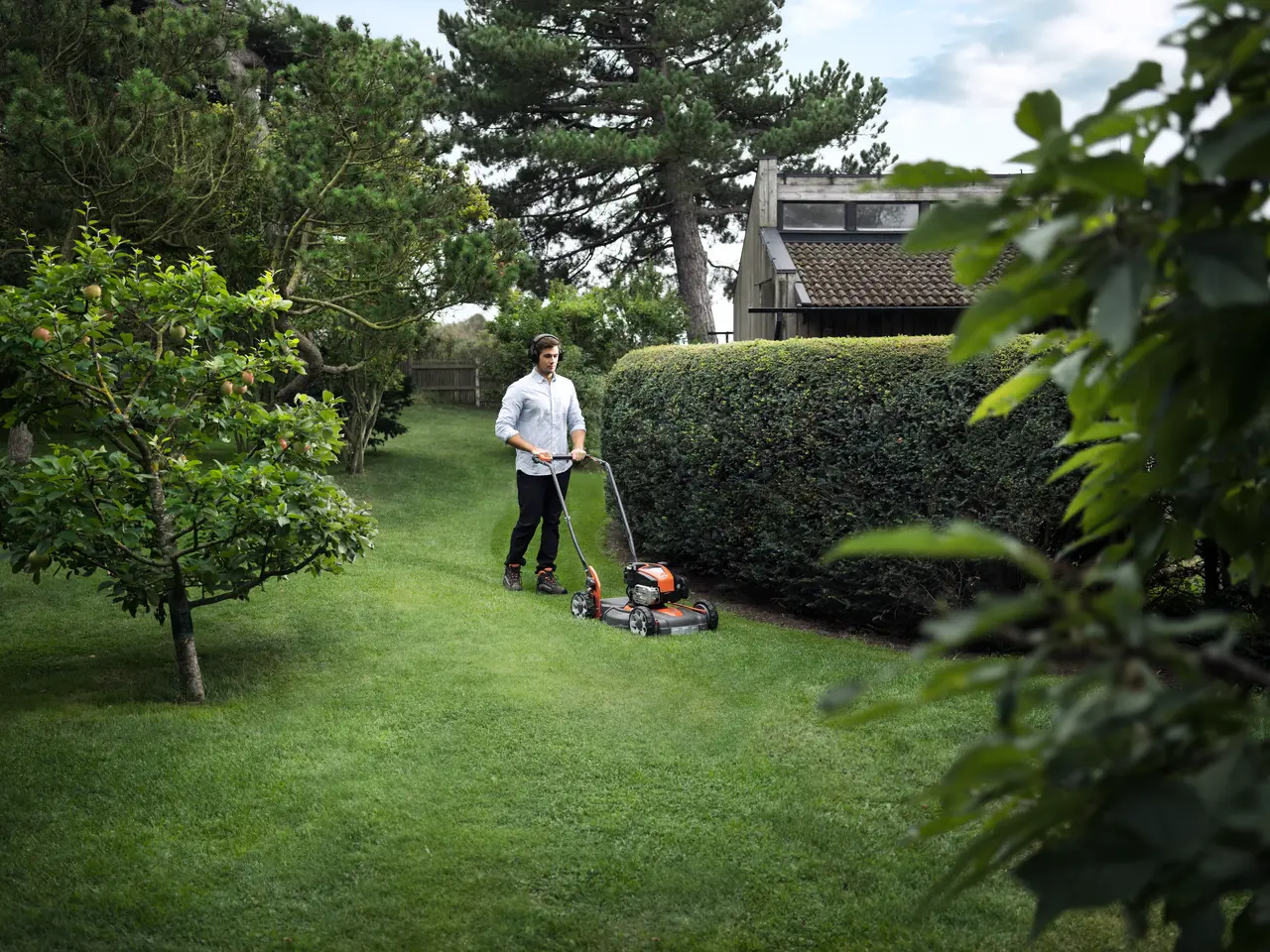 Mann som går med gressklipper i hage